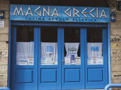Nel quartiere Picone, in via Lembo, si trova infine la taverna Magna Grecia. Gi� dalla facciata notiamo i colori blu e bianco della bandiera greca, che dominano anche il piccolo locale